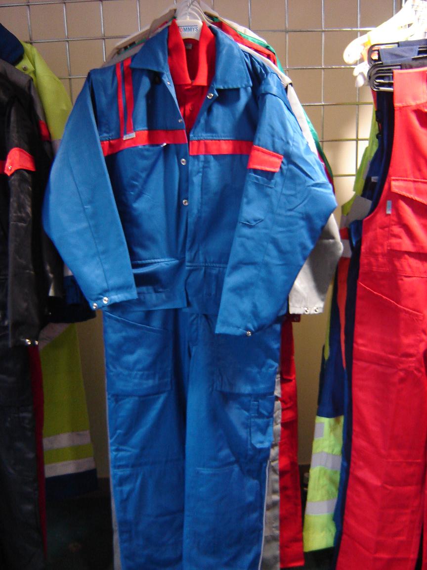 Niebieski kombinezon roboczy z czerwonymi akcentami, wiszący na wieszaku w Katowicach, widoczny na tle innych ubrań roboczych.